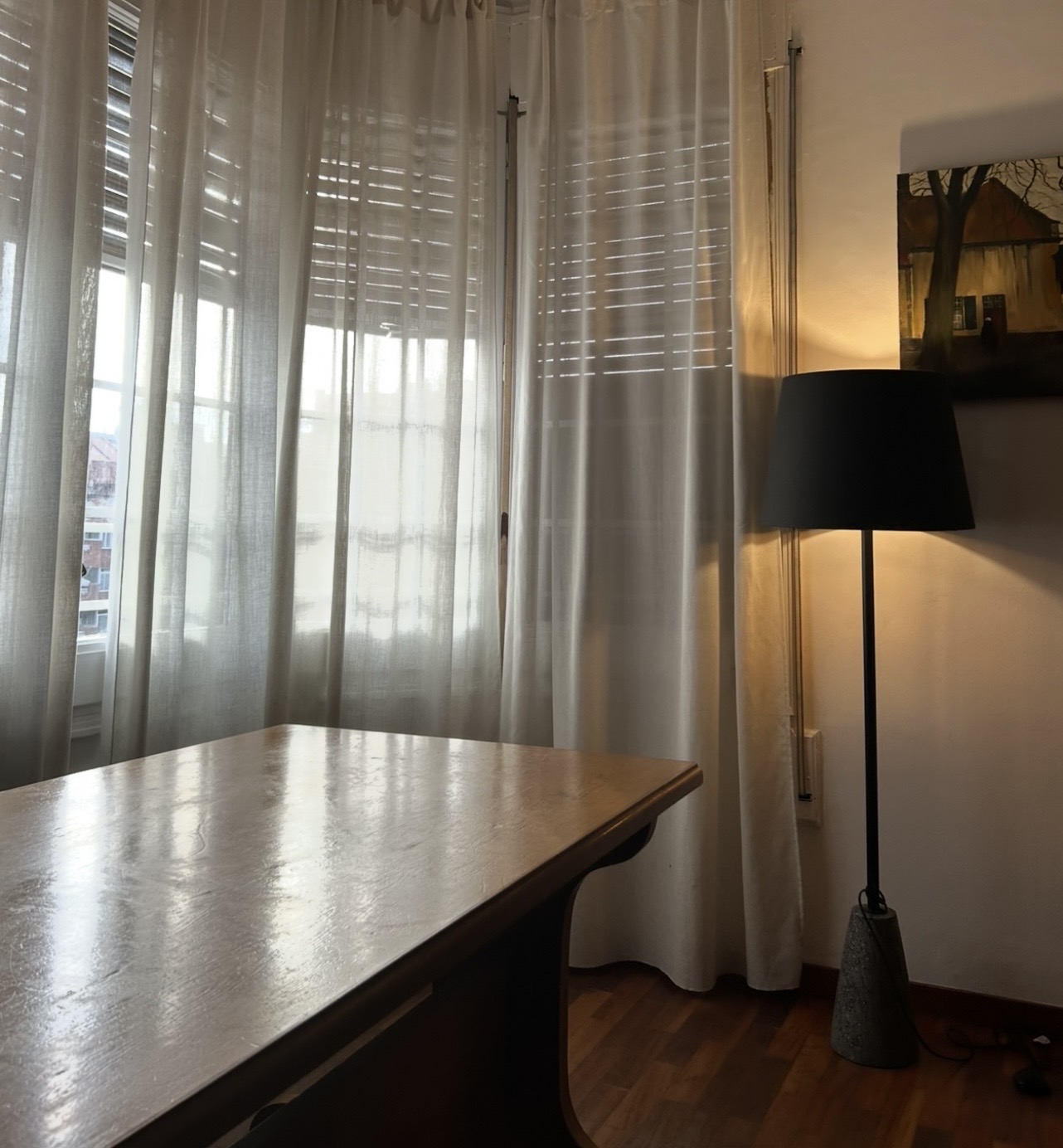 Consulting room with a wooden table, floor lamp and curtained windows